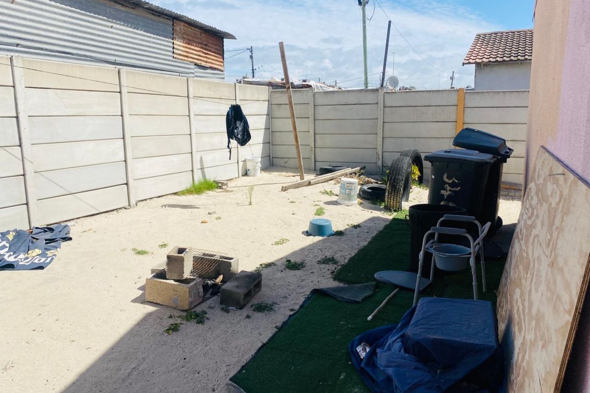 A rear yard area enclosed by precast concrete boundary walls, featuring a sandy surface and potential for landscaping or outdoor improvement.