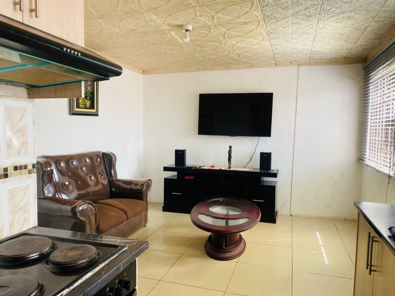 Open plan living area featuring tiled flooring, a textured ceiling, and an integrated kitchen section with an electric hob and extractor fan.