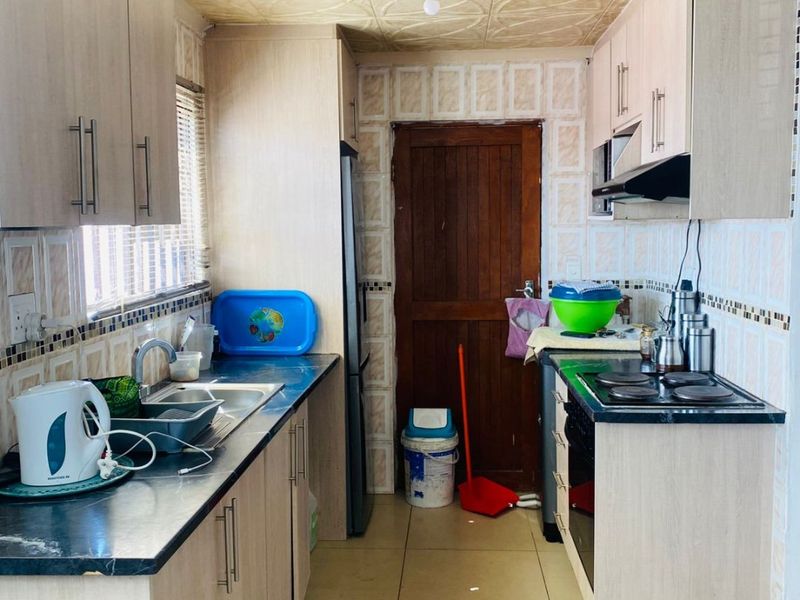 A functional galley-style kitchen featuring laminate cabinetry, dark countertops, built-in oven, electric hob, and tiled finishes throughout.