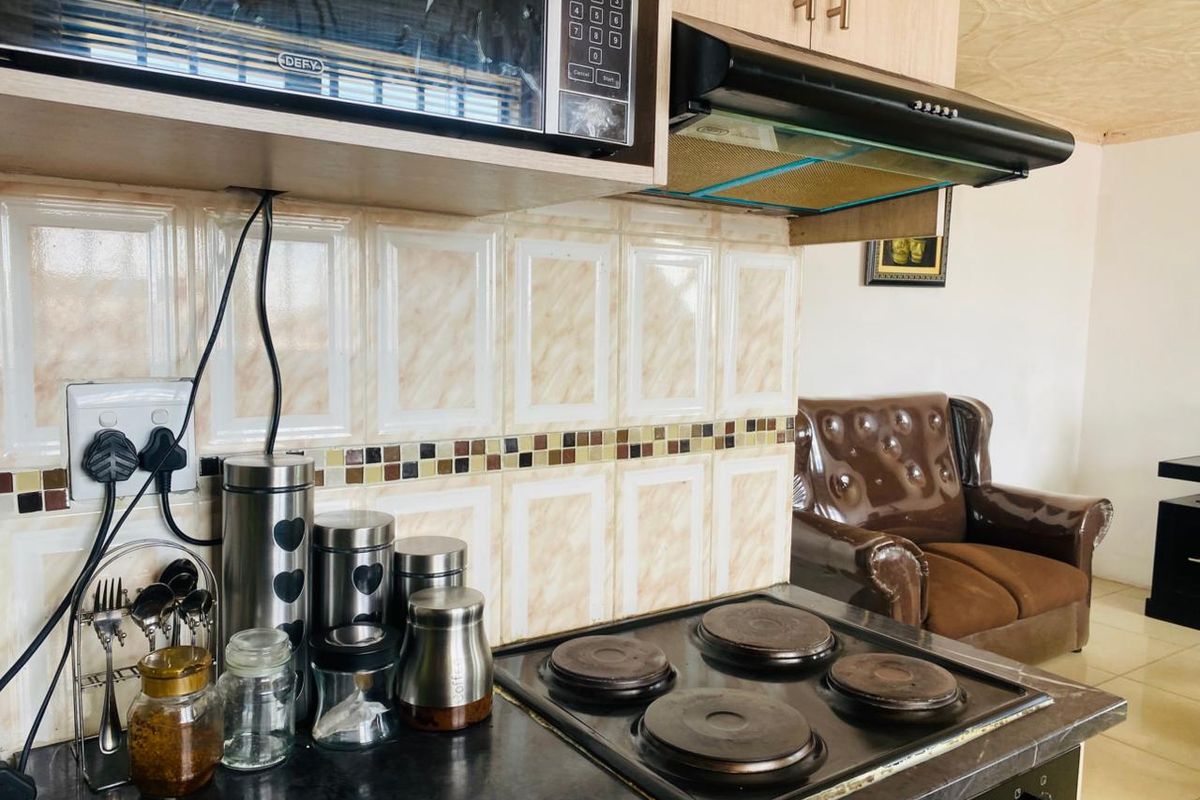 A functional kitchen area featuring a built-in microwave, extractor fan, electric hob, and decorative tiled backsplash with neutral cabinetry.
