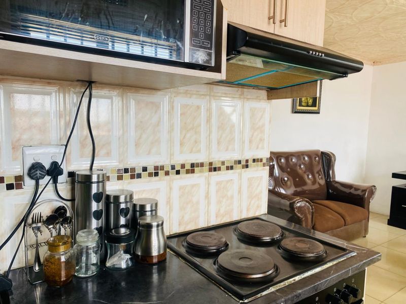 A functional kitchen area featuring a built-in microwave, extractor fan, electric hob, and decorative tiled backsplash with neutral cabinetry.