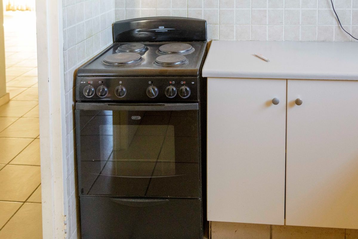 A compact kitchen area featuring a freestanding stove, laminate countertops, and tiled splashback, showing signs of age and wear.