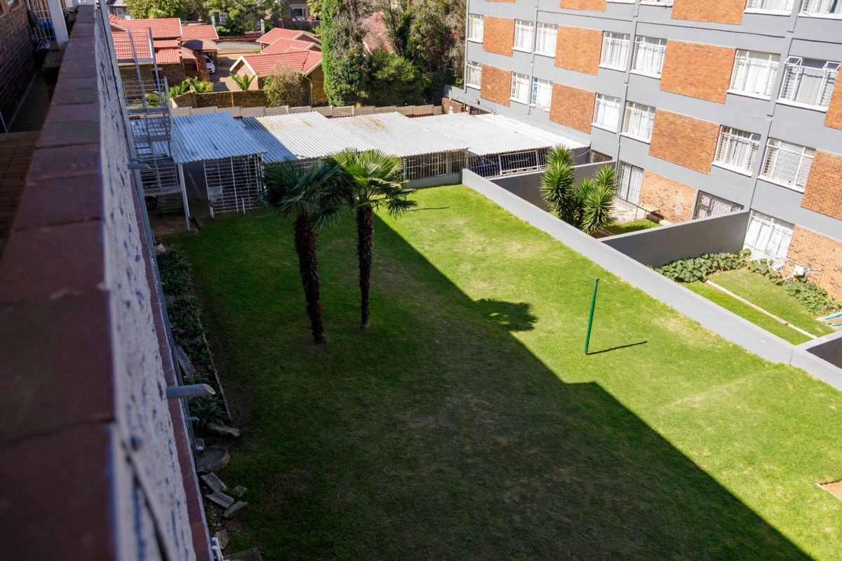 An elevated view of the communal rear garden area featuring a well-maintained lawn and boundary walls between apartment blocks.