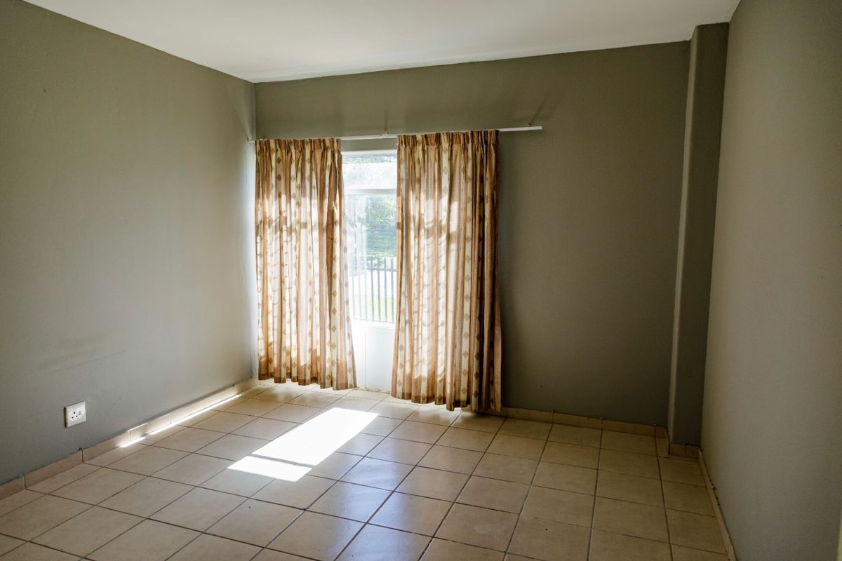 An empty bedroom featuring neutral wall paint, tiled flooring, and a window with a curtain rail.