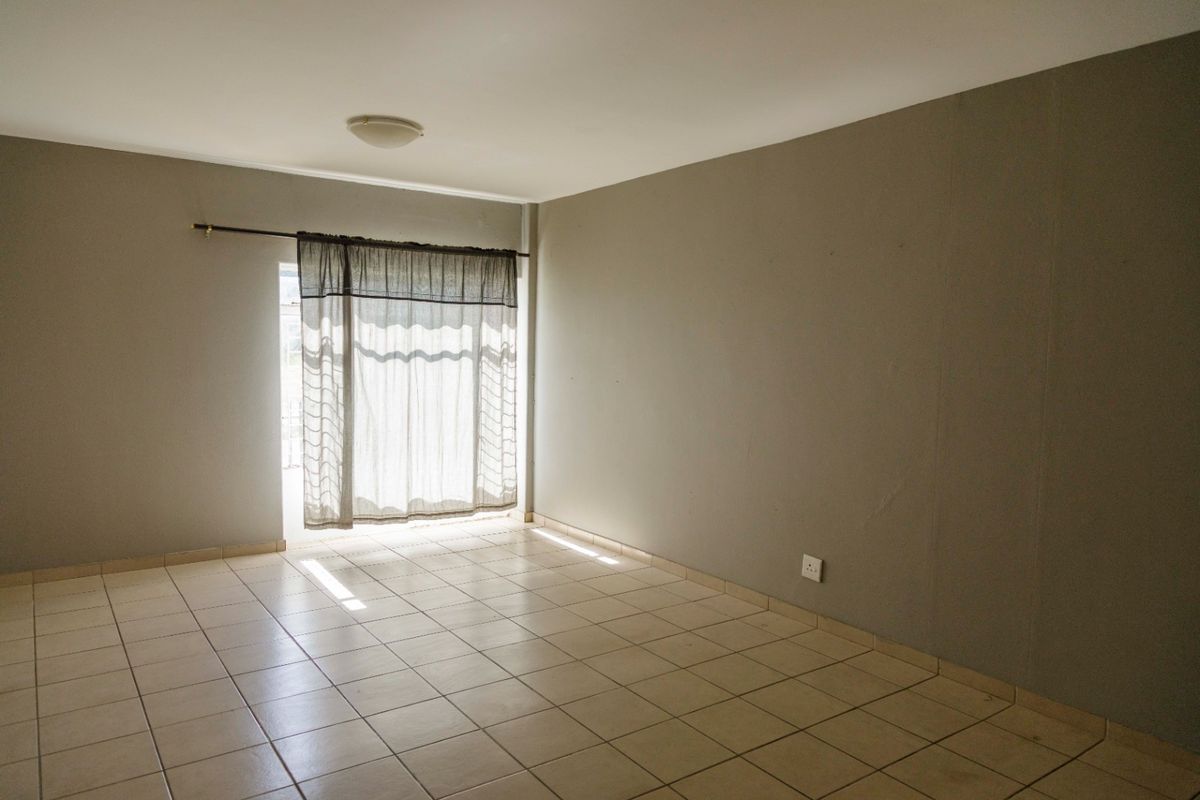 An empty living room featuring neutral tiled flooring, plain walls, and a sliding glass door providing natural light.