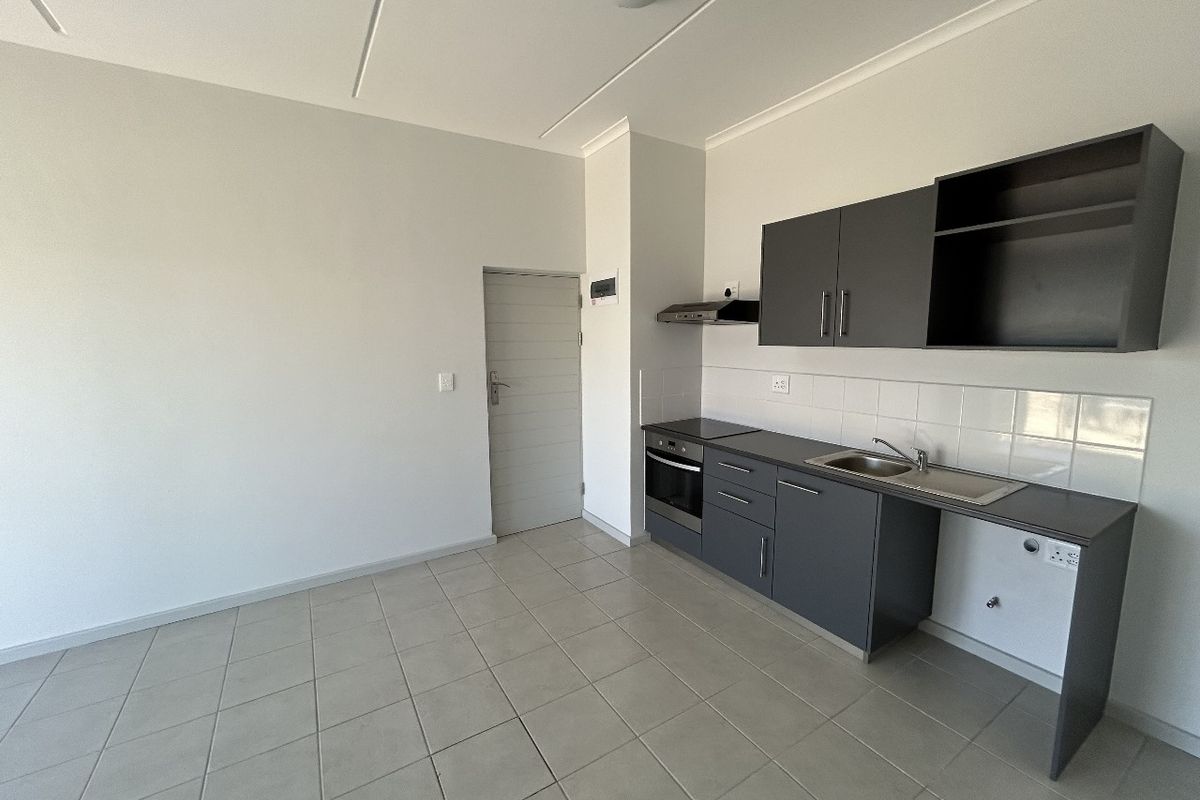 A clean, modern kitchen featuring dark grey cabinetry, built-in oven and hob, stainless steel sink, and neutral tiled flooring in an open-plan layout.