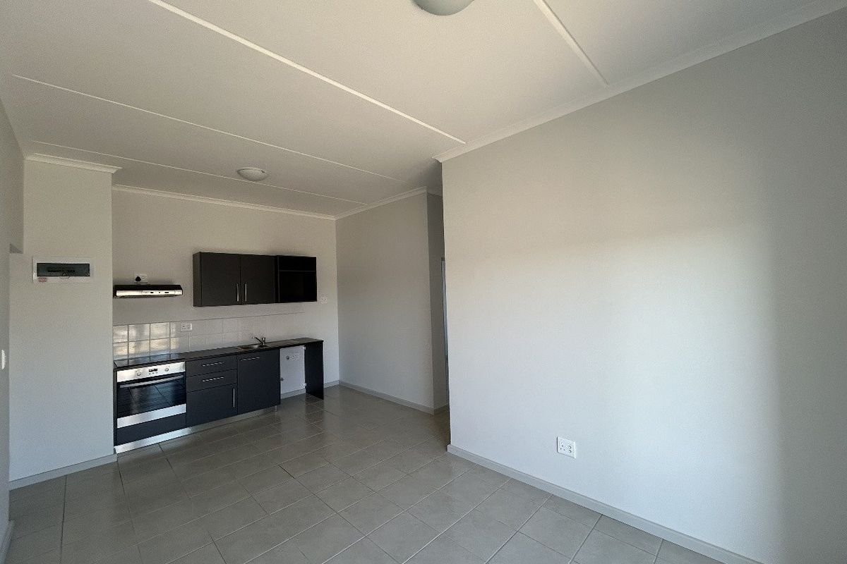 An open-plan living and kitchen area featuring tiled flooring, modern dark cabinetry, and built-in cooking appliances in a clean, vacant space.