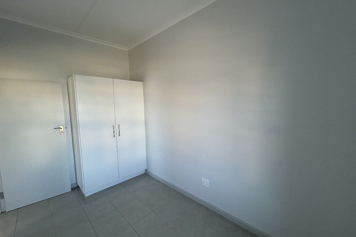 A clean, neutral bedroom featuring tiled flooring, a built-in wardrobe, and a standard interior door.