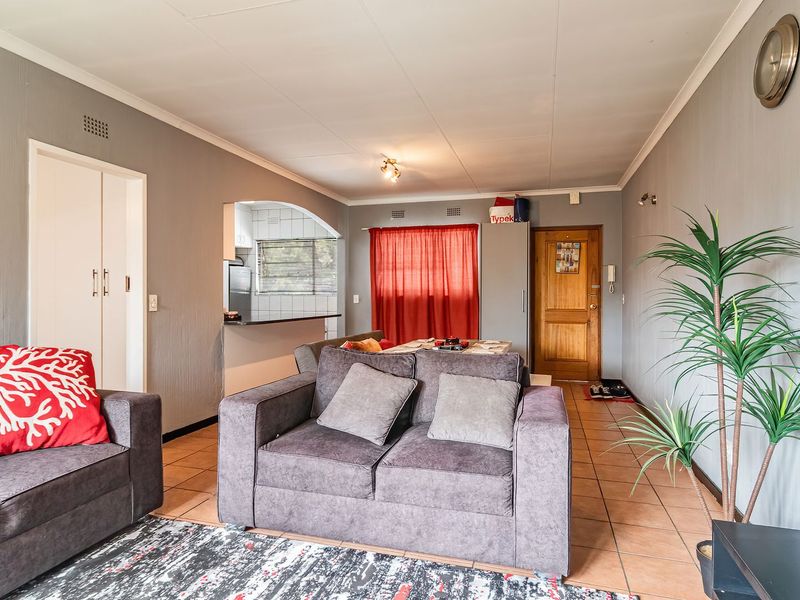 Open-plan living and dining area featuring tiled flooring, a pass-through kitchen window, and direct access to the main entrance.