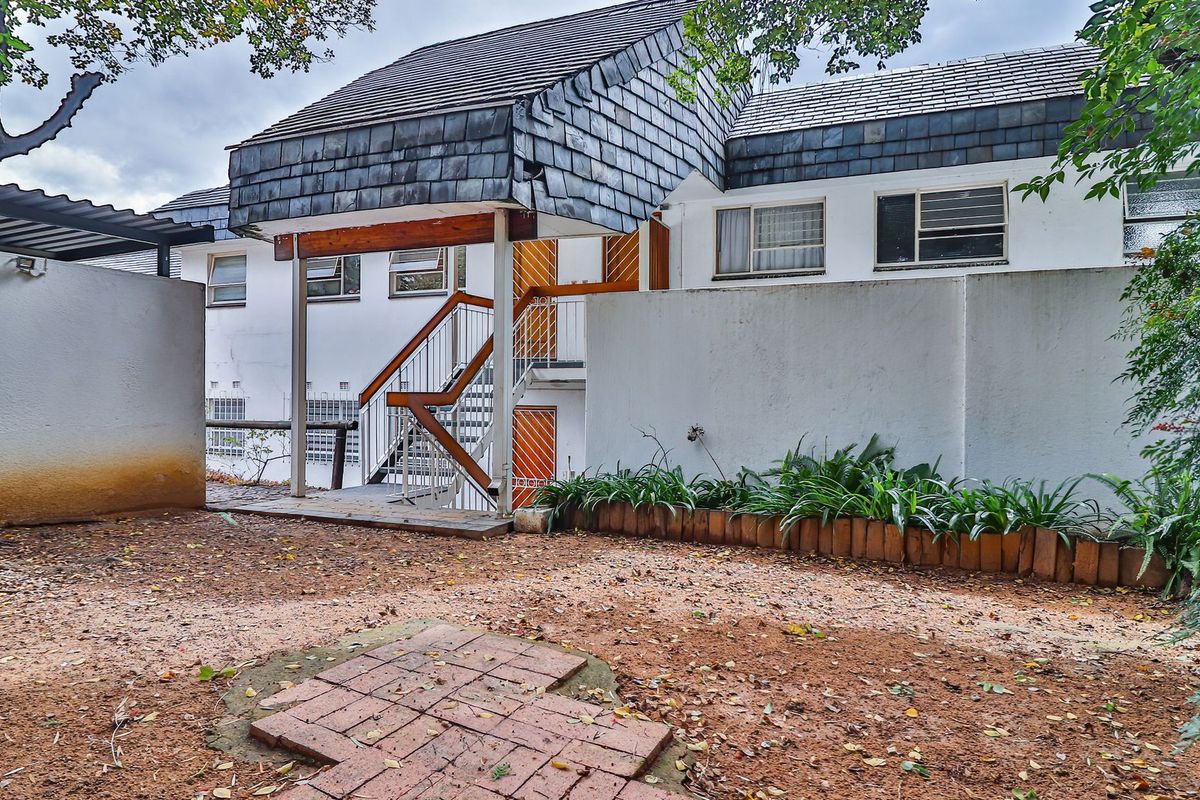Rear exterior view of the apartment building featuring a staircase, slate roof tiles, and a paved courtyard area requiring maintenance.