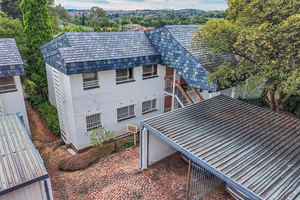 Aerial view of an apartment complex featuring a slate-tiled roof, paved driveway, and covered carport parking area.