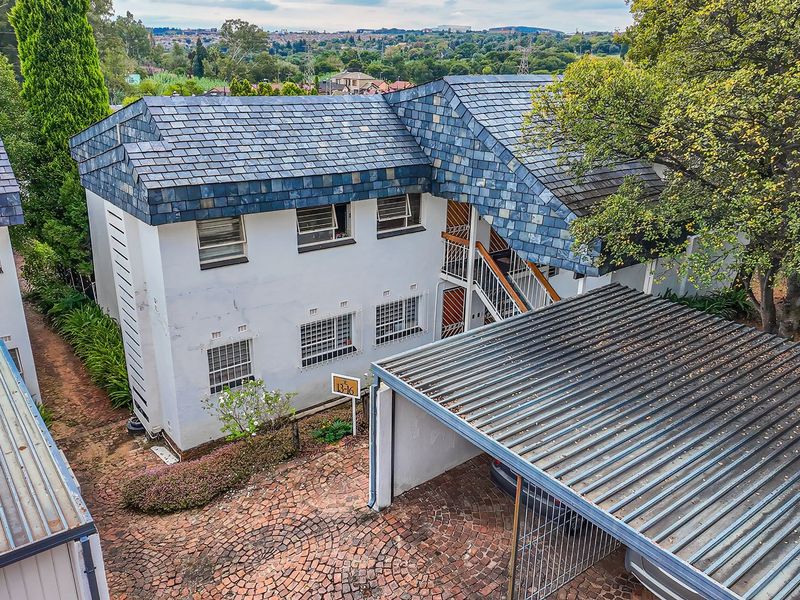 Aerial view of an apartment complex featuring a slate-tiled roof, paved driveway, and covered carport parking area.
