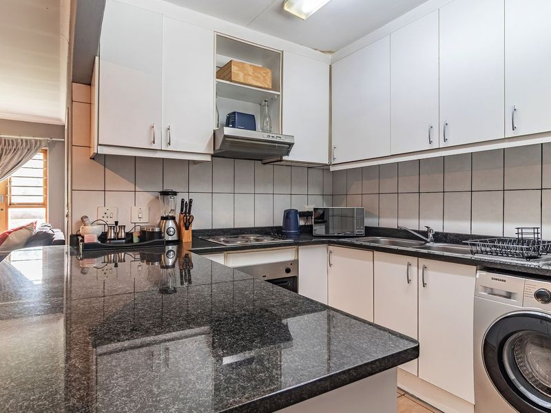 A functional kitchen featuring granite countertops, built-in cabinetry, a tiled backsplash, and integrated appliances including an oven, hob, and extractor fan.