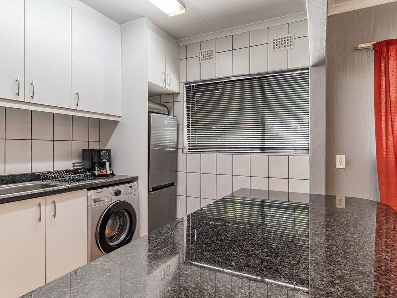 Functional kitchen featuring granite countertops, ample built-in cabinetry, a breakfast bar, and a tiled backsplash with integrated laundry plumbing.