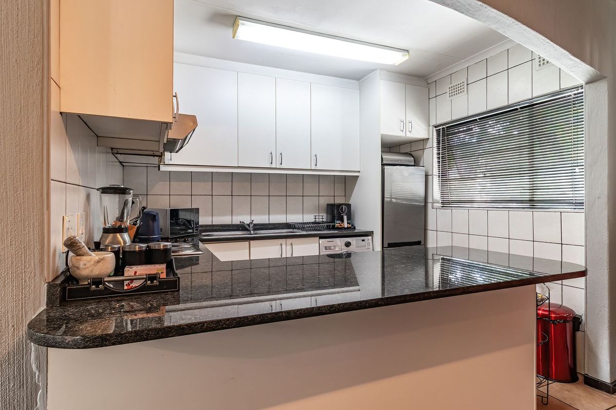 A functional kitchen featuring white cabinetry, granite countertops, a tiled backsplash, and a breakfast bar overlooking the living area.