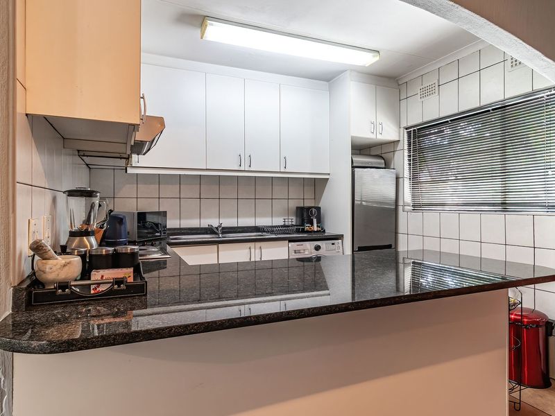 A functional kitchen featuring white cabinetry, granite countertops, a tiled backsplash, and a breakfast bar overlooking the living area.