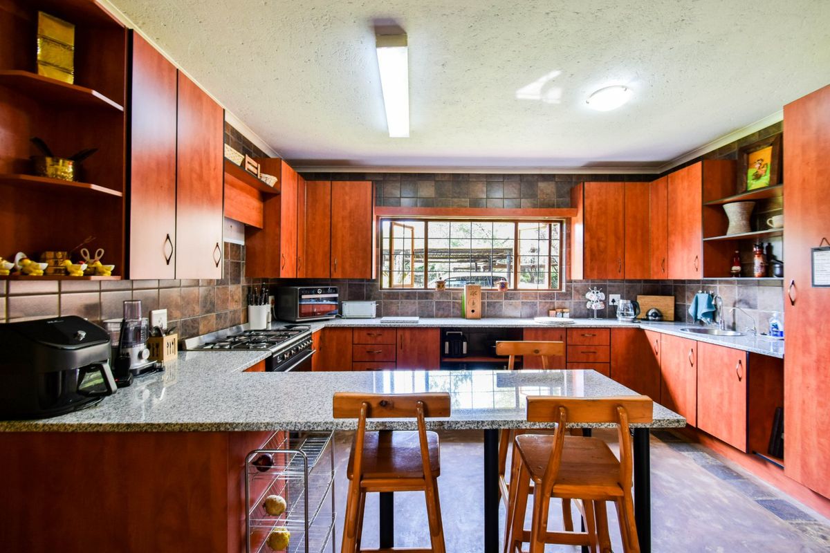 A functional kitchen featuring warm-toned cabinetry, granite countertops, a gas hob, and a tiled backsplash with a view through the window.