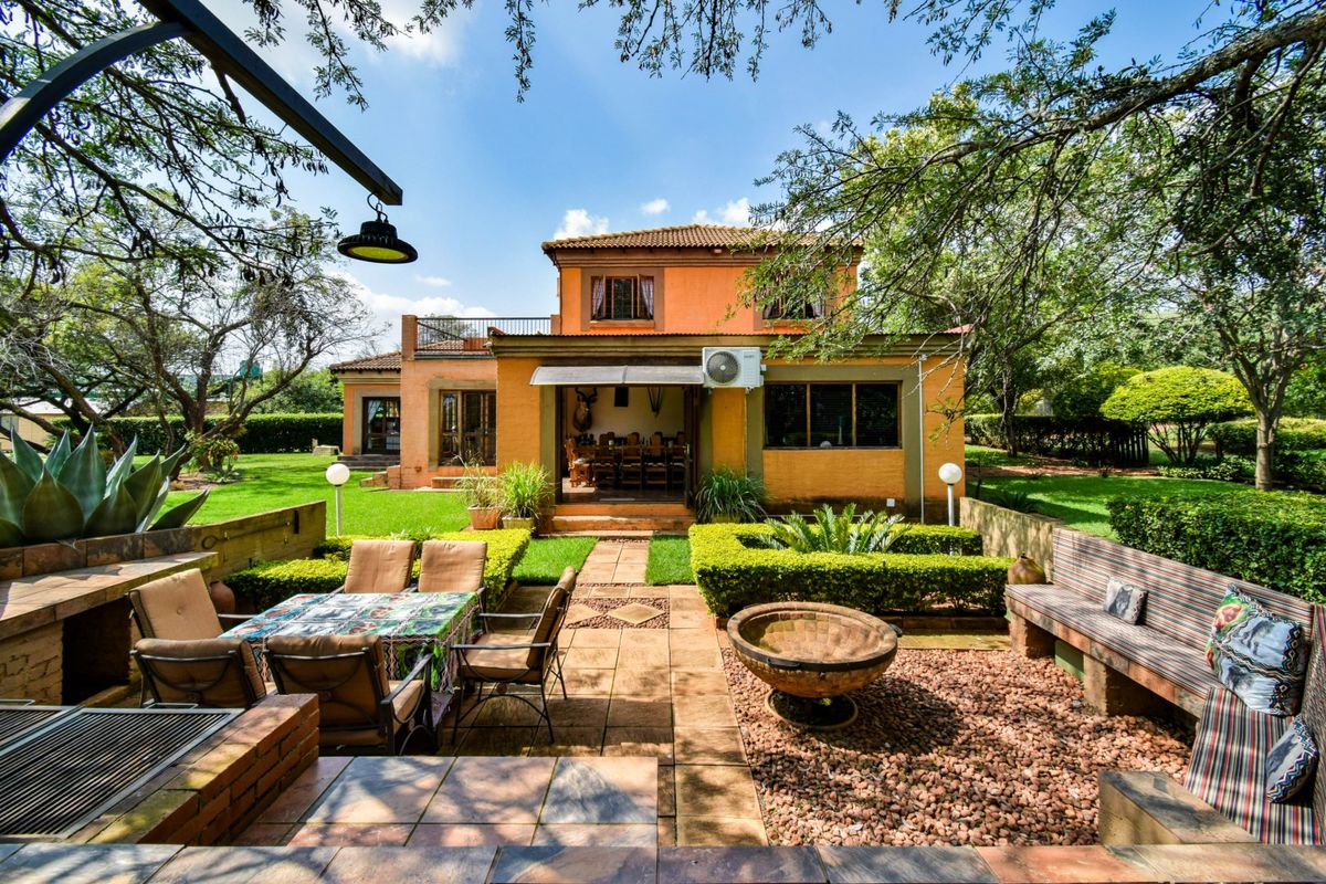 Rear view of a two-story farm house featuring a paved patio, built-in braai area, and a well-maintained garden.