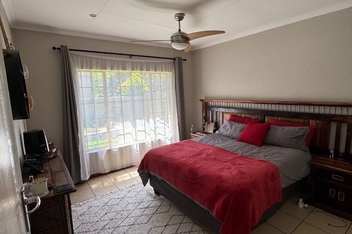 A well-lit bedroom featuring tiled flooring, a ceiling fan, and large windows with curtain rods, offering a comfortable and functional living space.