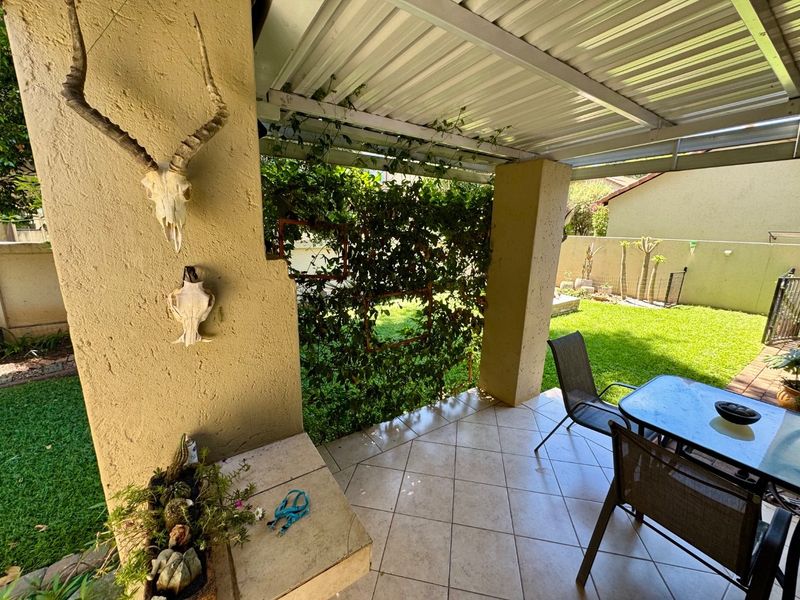 Covered patio area featuring tiled flooring, masonry pillars, and a built-in counter, overlooking a private garden space.