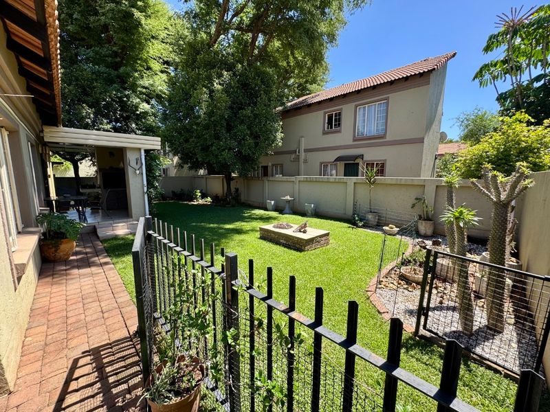 A well-maintained rear garden featuring a brick-paved walkway, a covered patio area, a built-in fire pit, and secure perimeter walling.