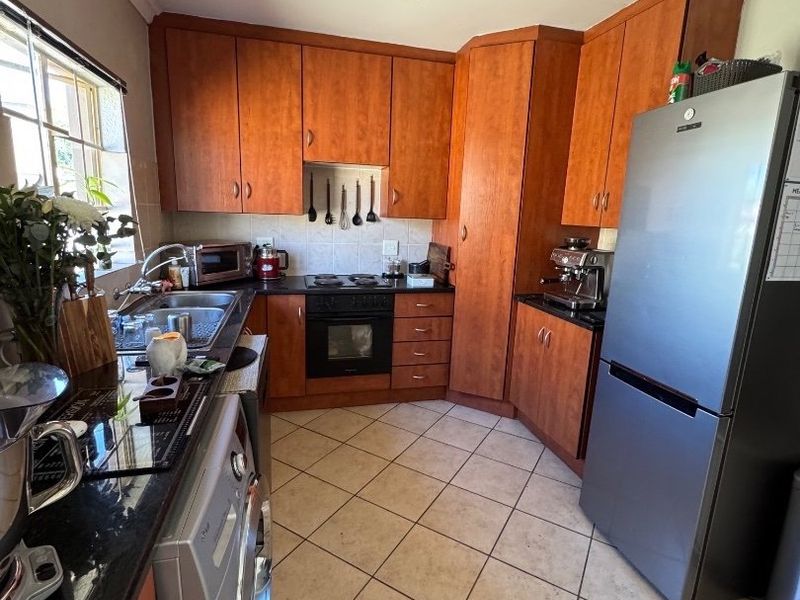 A functional kitchen featuring warm-toned wooden cabinetry, granite countertops, tiled flooring, and integrated appliances, offering a practical layout for daily meal preparation.