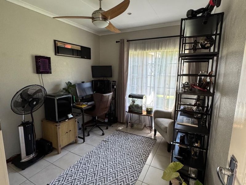 A functional home office space featuring tiled flooring, a ceiling fan, and a sliding glass door providing natural light.