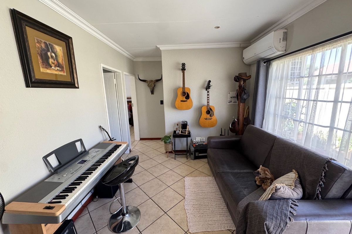A well-maintained living room featuring ceramic tiled flooring, coved ceiling cornices, and a wall-mounted split-system air conditioning unit.