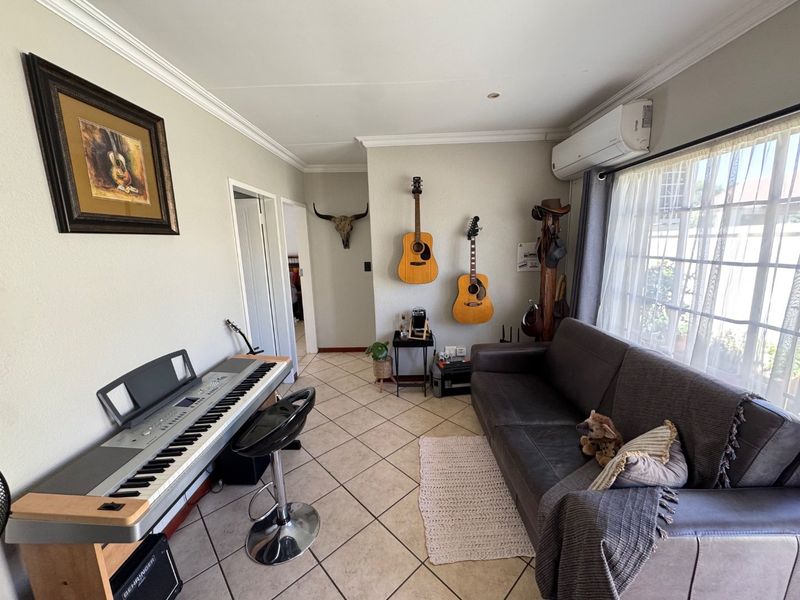 A well-maintained living room featuring ceramic tiled flooring, coved ceiling cornices, and a wall-mounted split-system air conditioning unit.
