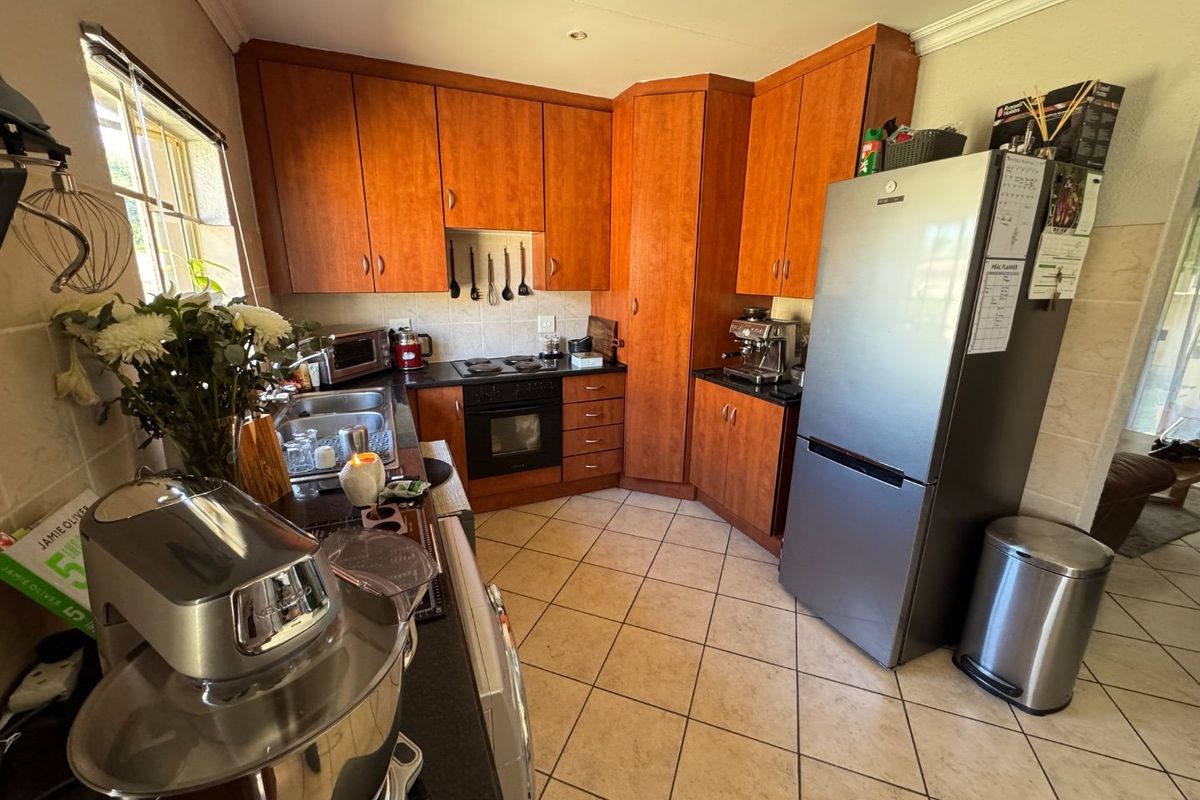A functional kitchen featuring wooden cabinetry, granite countertops, an electric hob, and an integrated oven with tiled flooring.