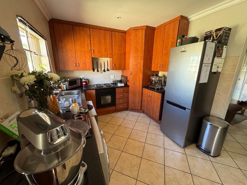 A functional kitchen featuring wooden cabinetry, granite countertops, an electric hob, and an integrated oven with tiled flooring.