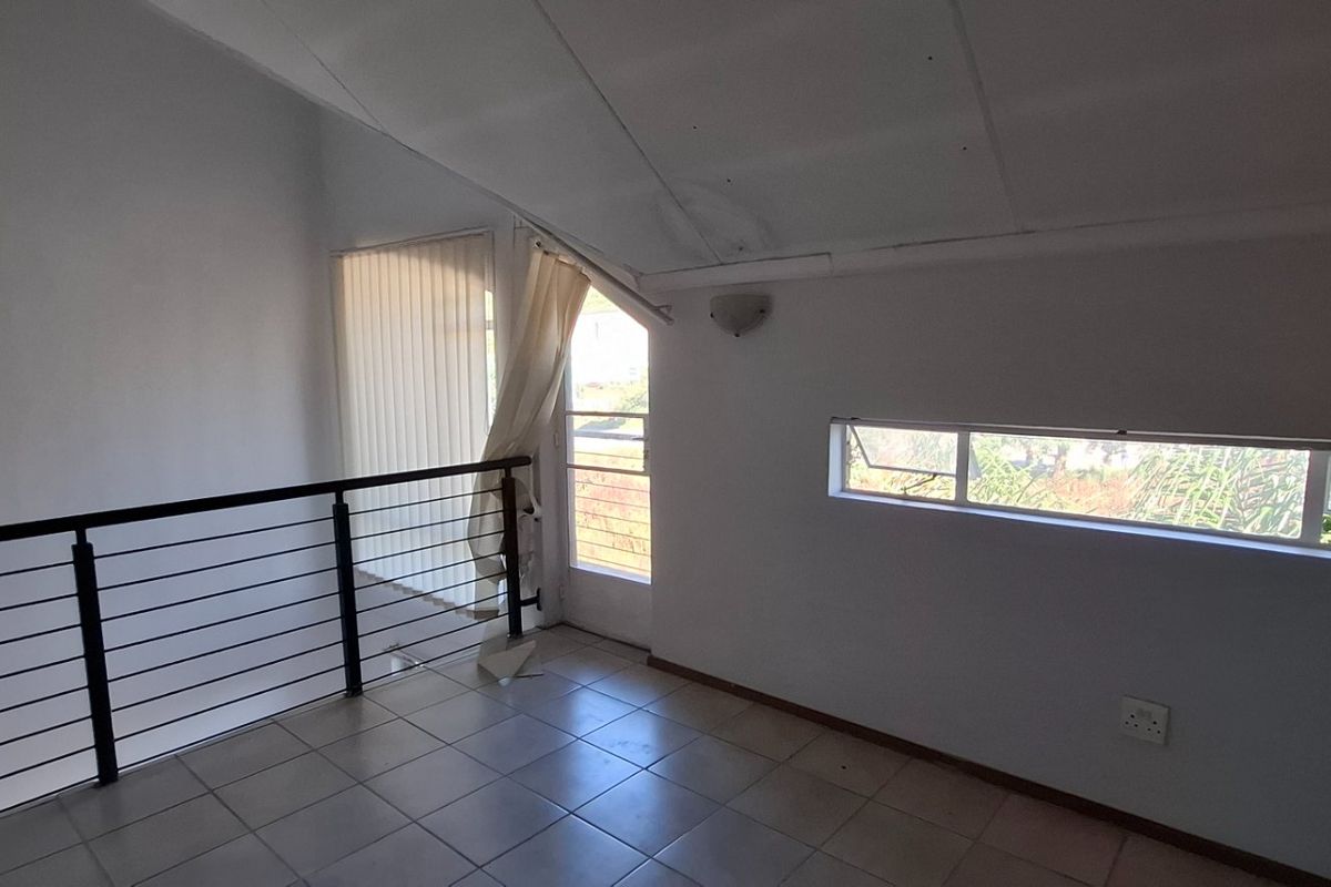 An empty, open-plan living area featuring tiled floors, a sloped ceiling, and a metal balustrade overlooking the lower level.