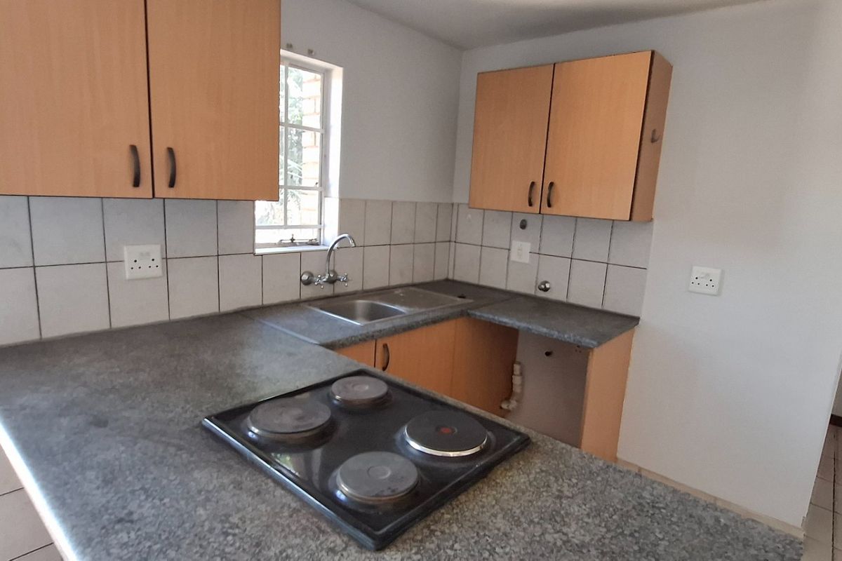 A functional kitchen featuring laminate cabinetry, a stone-look countertop, an integrated electric hob, and a stainless steel sink with tiled splashback.