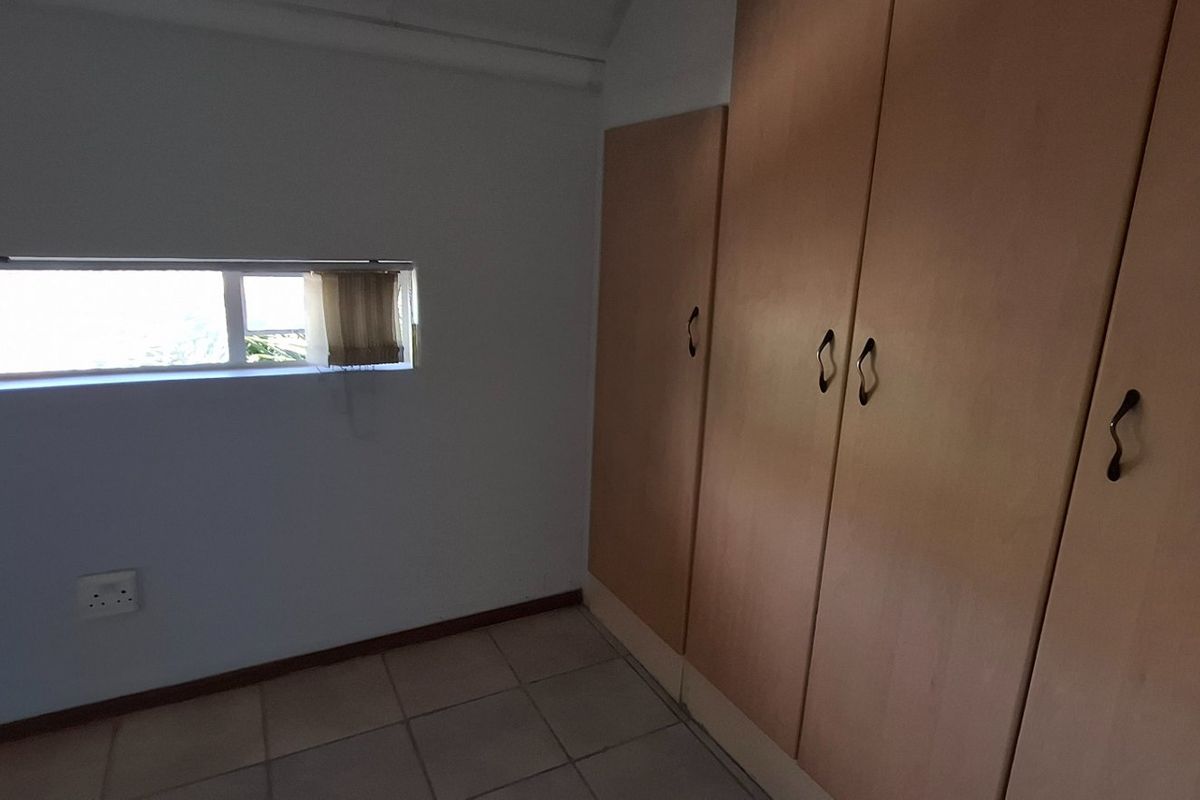 An empty bedroom featuring tiled flooring and built-in wooden cupboards with a horizontal window.