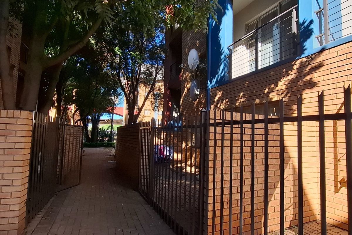 Exterior view of an apartment complex featuring face brick walls, metal security fencing, and a paved walkway leading between building blocks.