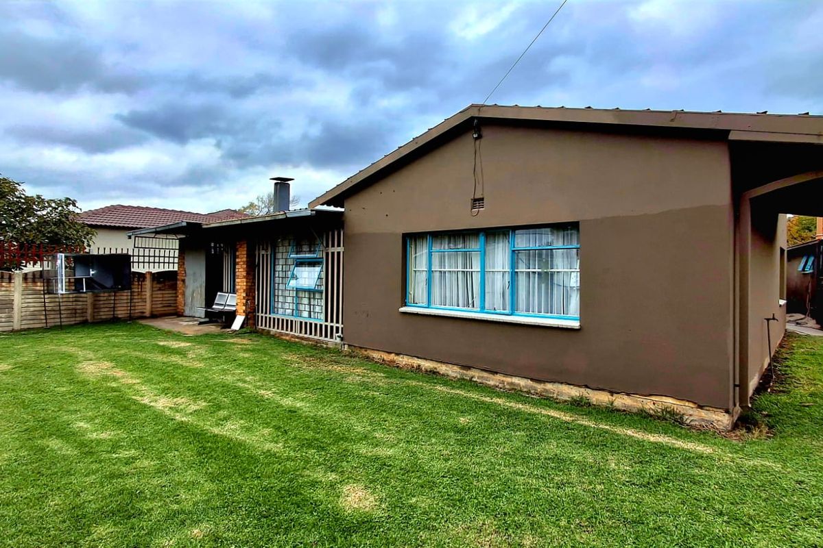 Rear view of the house featuring a lawn, concrete boundary wall, and exterior walls with metal security bars on the windows.