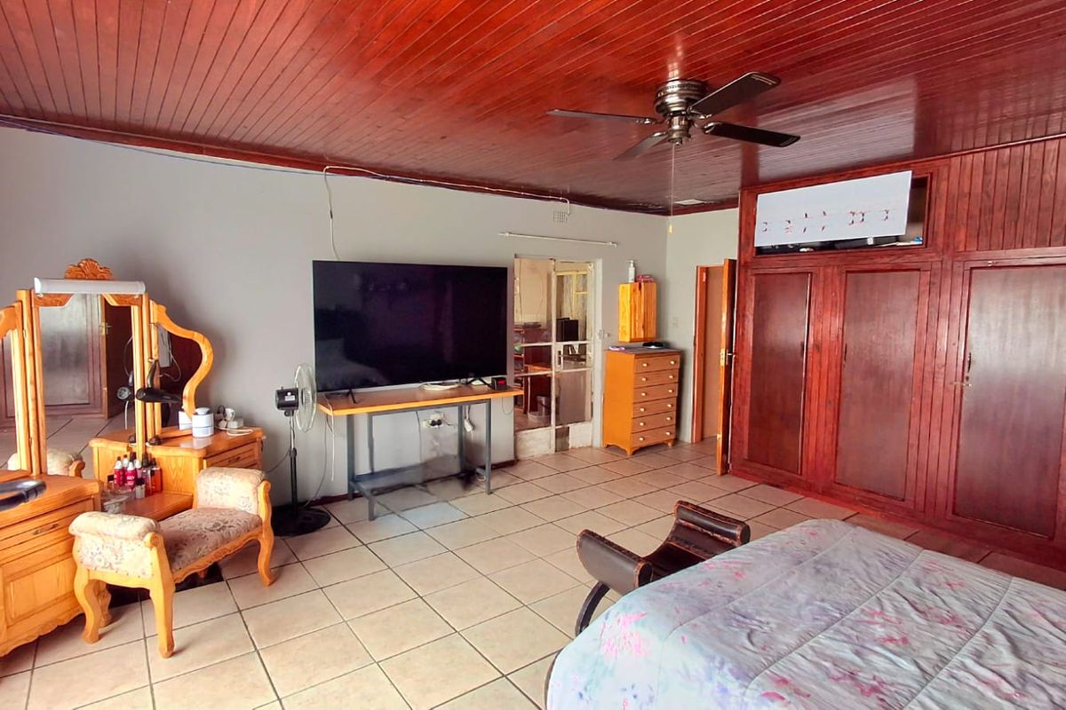 Spacious bedroom featuring tiled flooring, built-in wooden cabinetry, and a classic wooden paneled ceiling with an integrated fan.