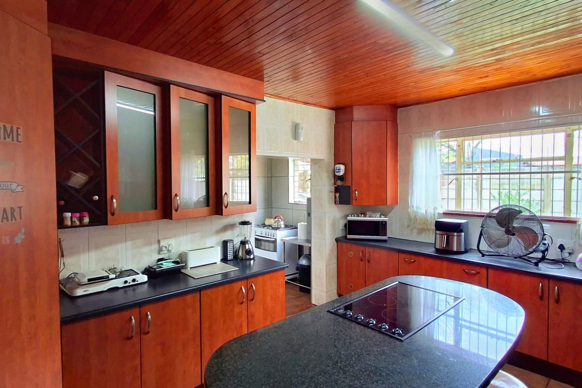 A functional kitchen featuring wooden ceiling paneling, granite countertops, a central island with an integrated electric hob, and ample built-in cabinetry.