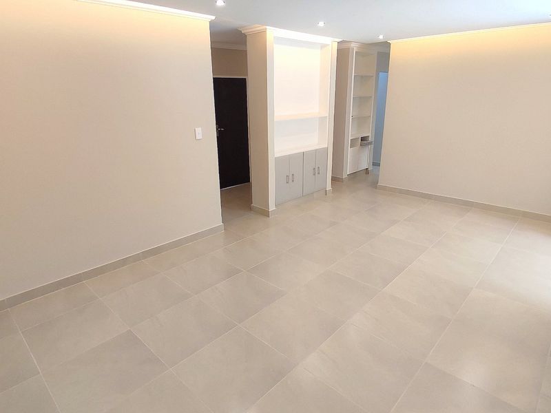 A bright, spacious, and empty living area featuring neutral tiled flooring, recessed ceiling lighting, and built-in cabinetry.