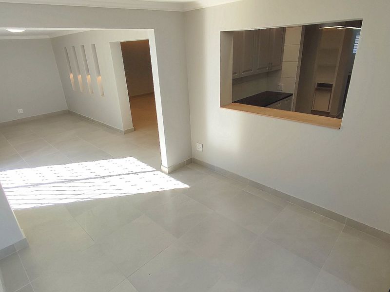 A bright, vacant open-plan living area featuring neutral tiled flooring, decorative wall niches, and a convenient serving hatch connecting to the kitchen.