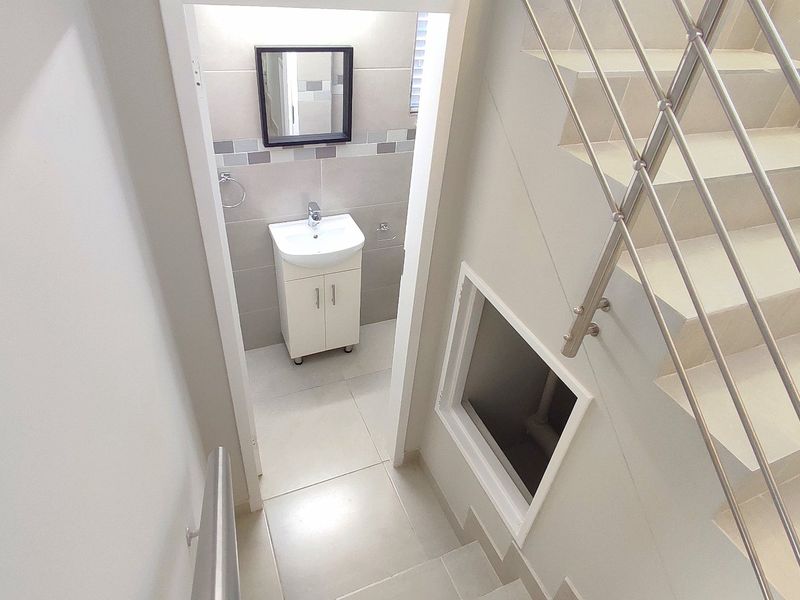 A clean, modern bathroom featuring a vanity cabinet and basin, situated adjacent to a tiled staircase with a stainless steel railing.