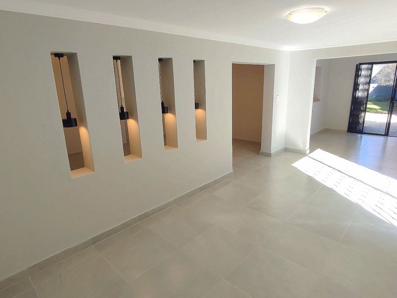 Bright open-plan living area featuring neutral tiled flooring, modern recessed wall niches with pendant lighting, and direct access to the outdoor patio area.