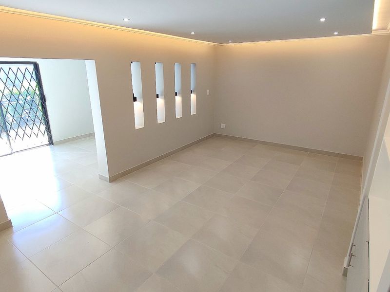 A bright, modern living area featuring neutral tiled flooring, recessed cove lighting, and decorative wall niches, leading to an outdoor access point.