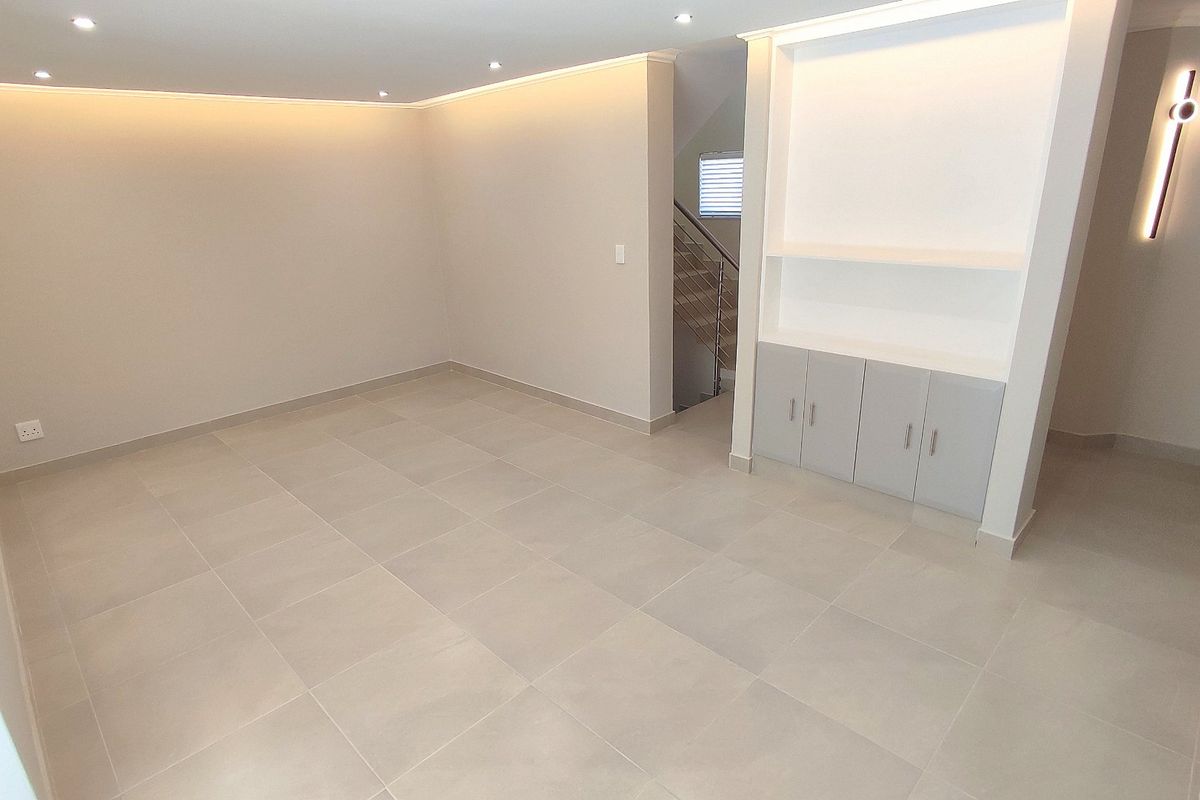 A bright, modern, and empty living area featuring neutral tiled flooring, recessed ceiling lighting, and custom built-in cabinetry with integrated shelving.