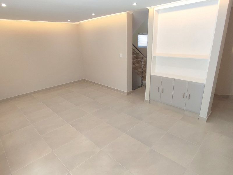 A bright, modern, and empty living area featuring neutral tiled flooring, recessed ceiling lighting, and custom built-in cabinetry with integrated shelving.