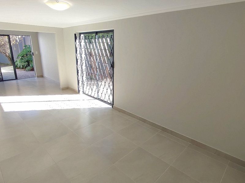 A bright, empty living area featuring neutral tiled flooring and sliding glass doors with security gates leading to an outdoor space.