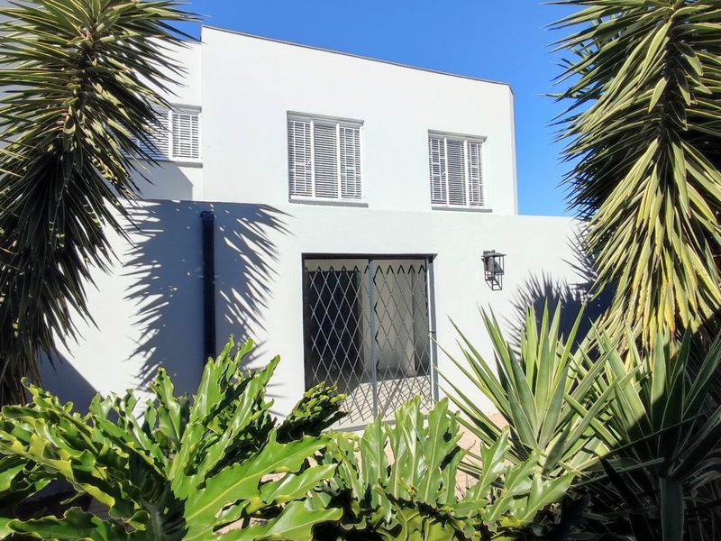 Rear elevation of the townhouse featuring white rendered walls, window shutters, and a secure metal gate entrance framed by established garden foliage.