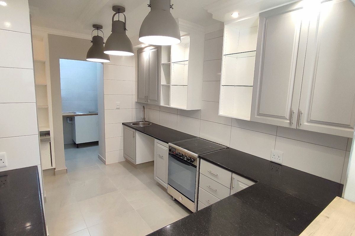 Modern kitchen featuring sleek grey cabinetry, dark granite countertops, stainless steel oven, and contemporary pendant lighting, with an adjacent scullery area.