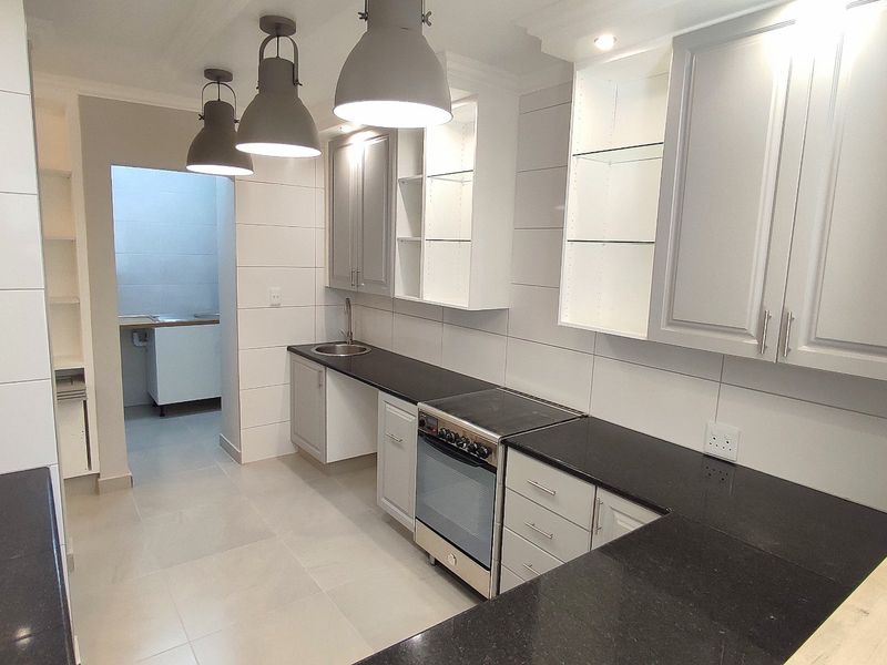 Modern kitchen featuring sleek grey cabinetry, dark granite countertops, stainless steel oven, and contemporary pendant lighting, with an adjacent scullery area.