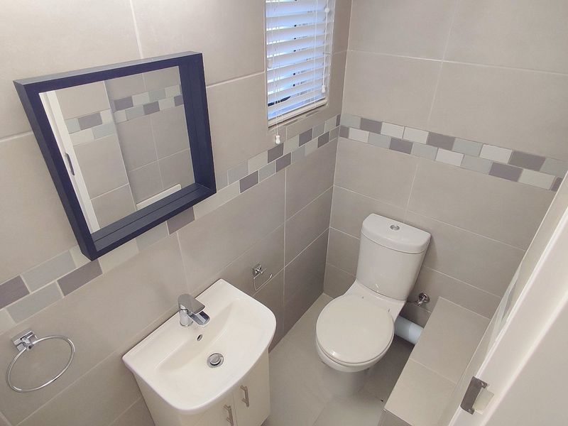 A compact, modern guest bathroom featuring neutral wall tiles, a wall-mounted vanity basin, and a dual-flush toilet.